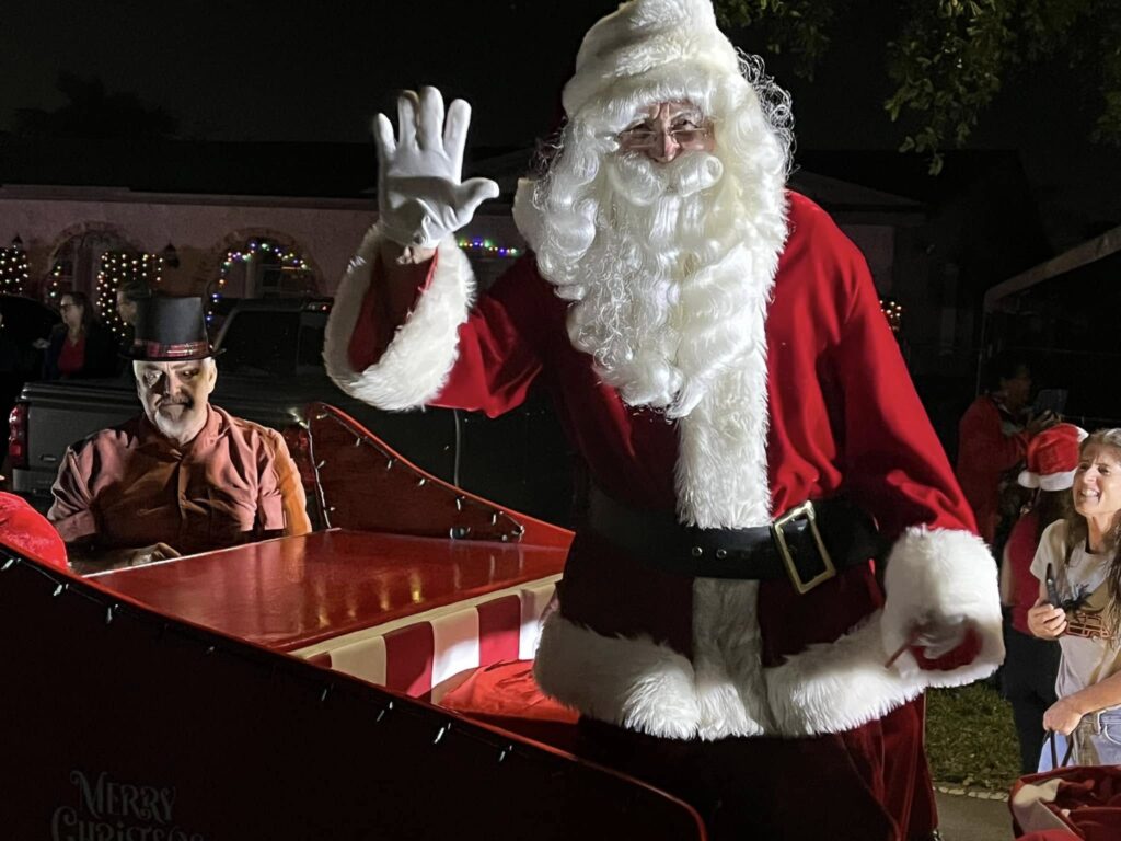 Santa in his red suit waving from the red sleigh after dark