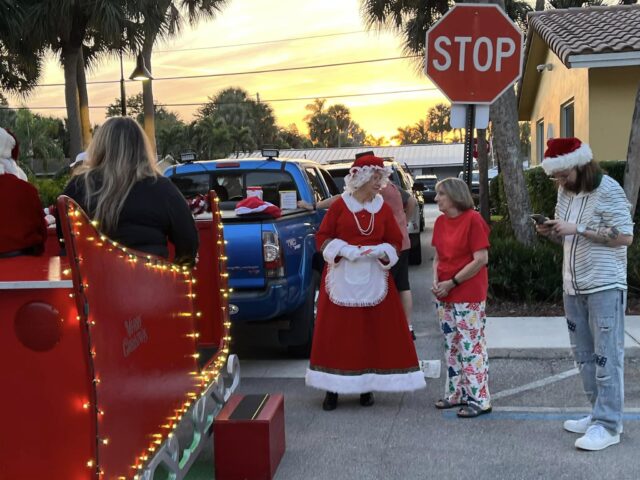 Mrs. Claus and helpers beside the lit red sleigh in the late afternoon