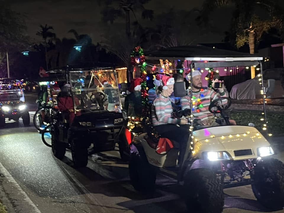 A line of decorated golf carts with lights driving behind the sleigh at night