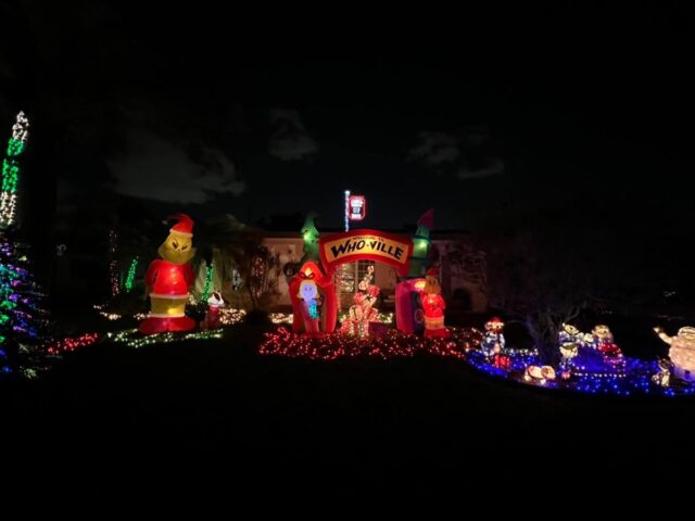 A yard with a Santa’s workshop inflatable and lights at night